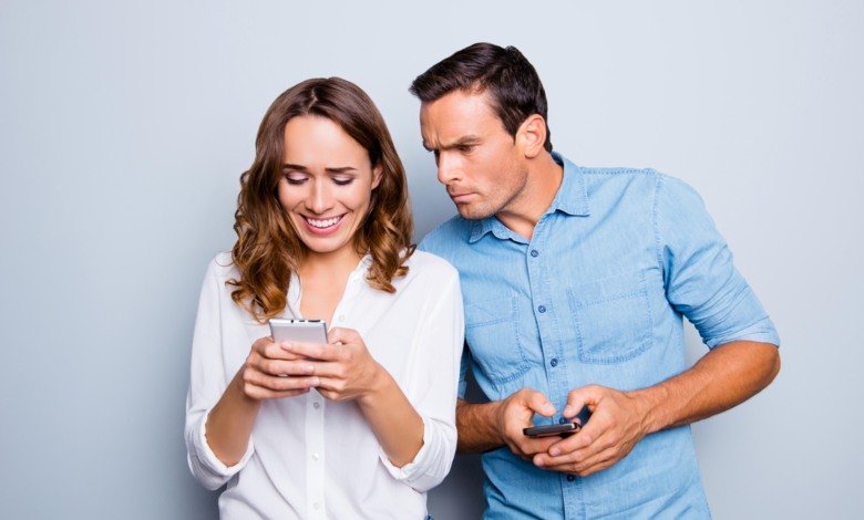 Picture of a man looking at the woman's phone over her shoulder and getting jealous.