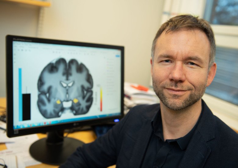 Porträtt av Andreas Olsson framför en bildskärm med en hjärna avbildad.