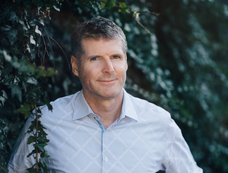 Portrait of Peder Olofsson in front of green bushes and dressed in a light-blue shirt.