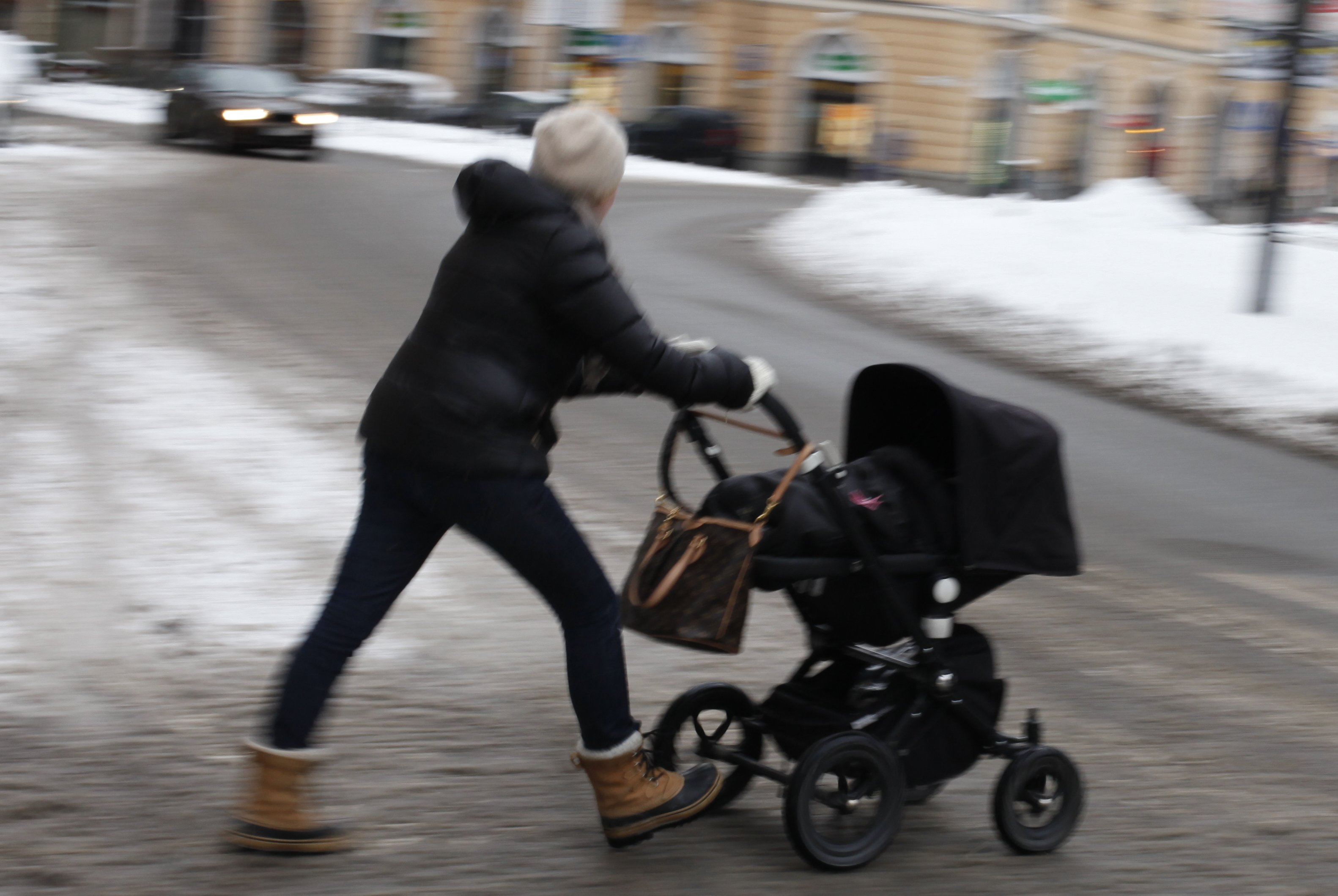 Kvinna går över gatan med barnvagn