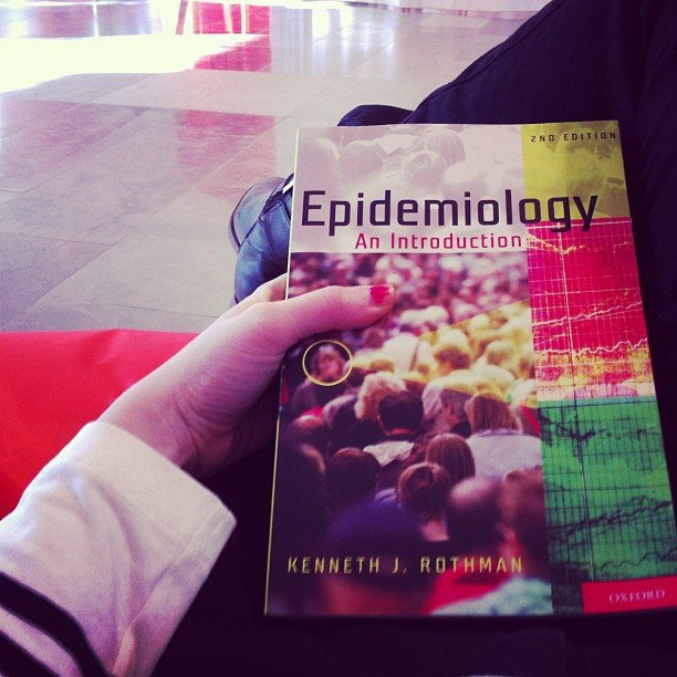 Läroboken Epidemiologi i en students hand