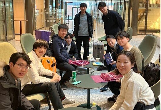 9 Japanese students sitting in green armchairs looking into the camera and smiling.