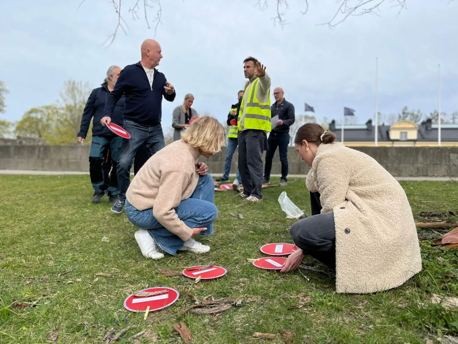 En grupp människor står på en gräsplan och tittar på små runda plattor. En person har en reflexväst.