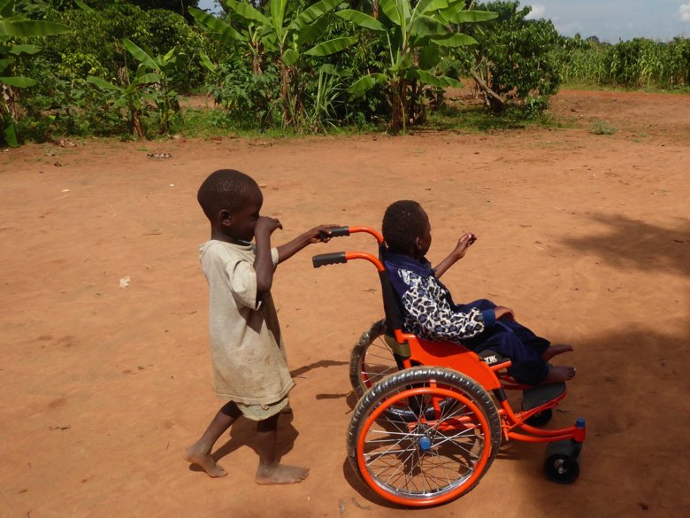 Child pushing another child in a wheelchair in Uganda