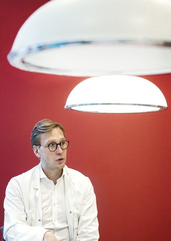 Bild på Mathias Svahn sittandes framför en röd vägg.