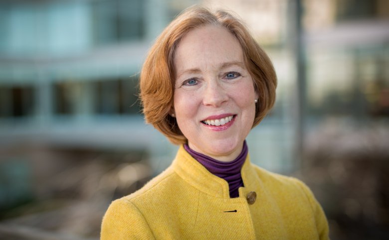 Portrait of Cynthia Bulik, she has red hair and a yellow jacket.