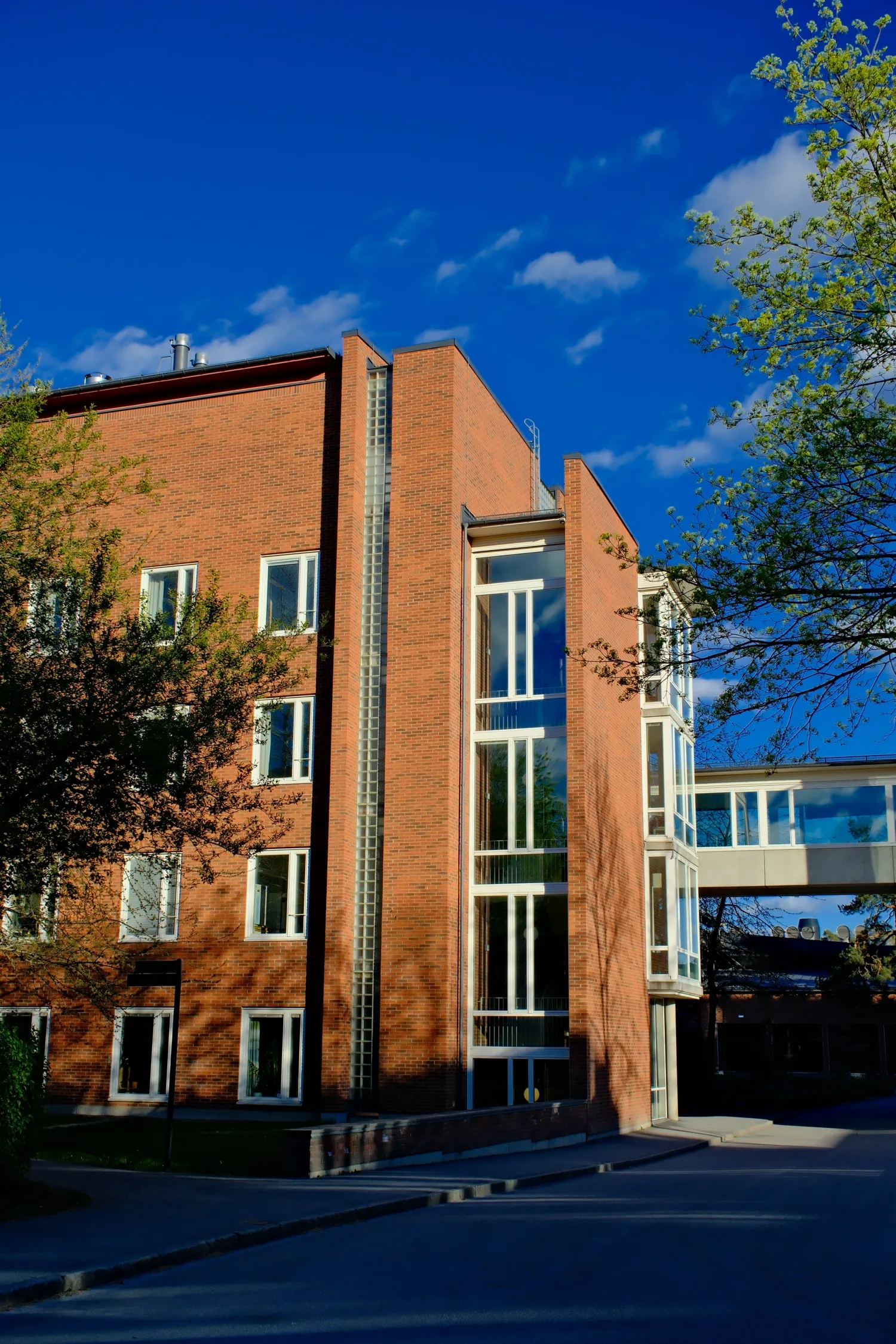 A modern research laboratory surrounded by green trees and open spaces under a clear blue sky. The image conveys a calm and inspiring academic environment focused on research, innovation, and nature.