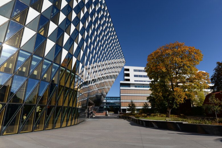 Glasfasaden på Aula Medica. Bredvid står ett stort träd med färgglada löv.