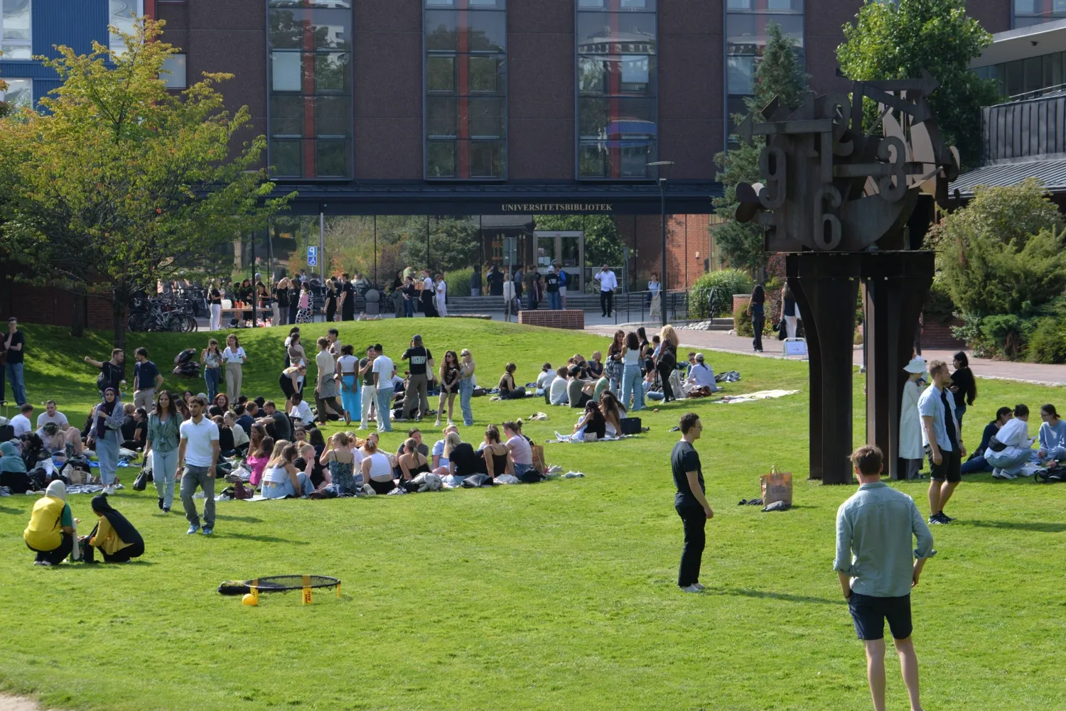 Studenter som hänger på gräsmattan utanför KIB på campus Solna under mottagningen hösten 2024.