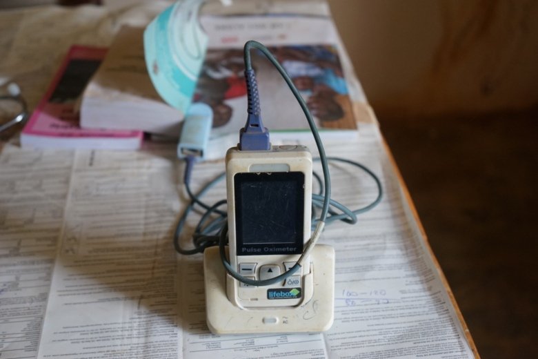 An Pulse Oximeter standing on a table on papers. In the background books and images.