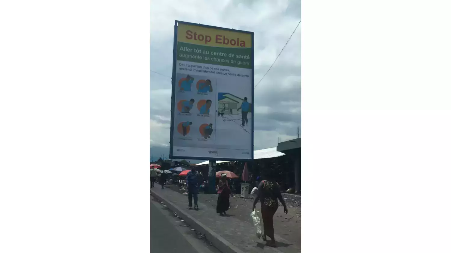 Skylt med information om Ebola längst en gata med bilar, människor och hus i DR Kongo.