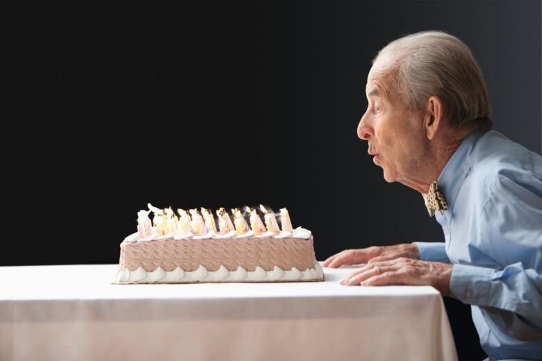 Old man blowing out candles on birthday cake