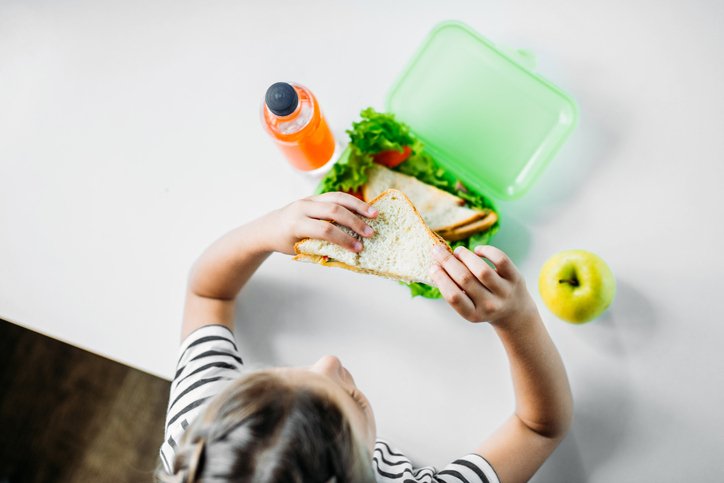 Kid eating a sandwich from a lunch box. In the background you can see an apple and sallad.