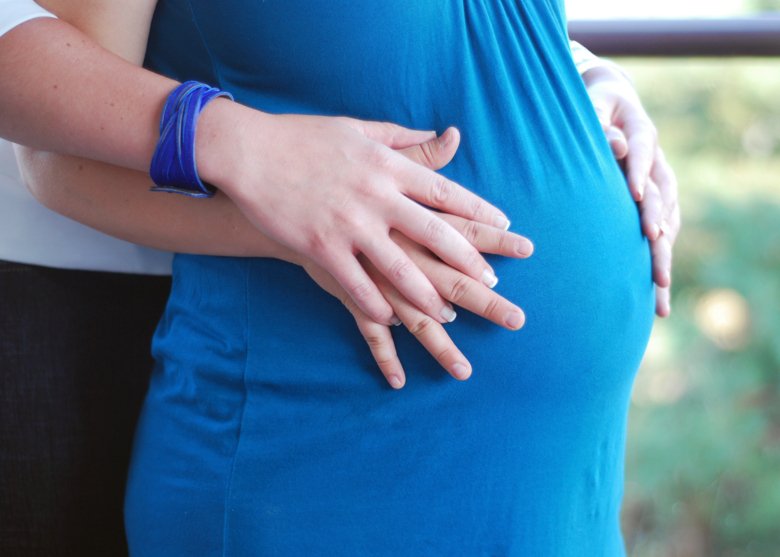 Close up of two women holding hands over a pregnant woman's belly