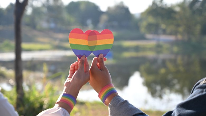 Homosexuellt par som håller upp två regnbågsfärgade hjärtan