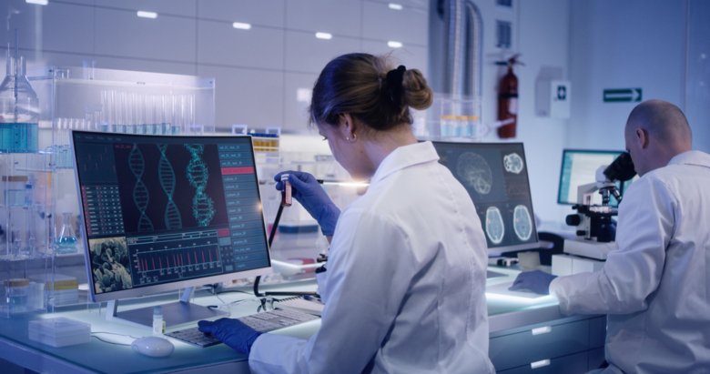 Researcher examines test tube in front of computer.