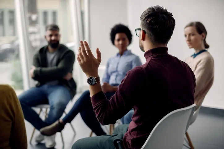 People sitting in a circle and man raising his hand.