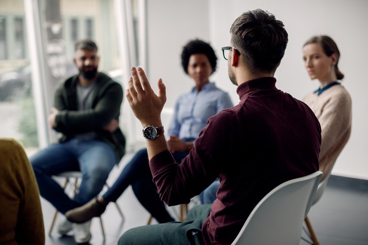 People sitting in a circle and man raising his hand.