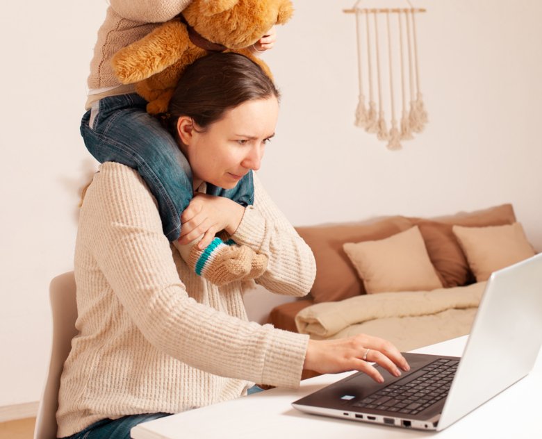 A mother sitting at the computer with her daughter on her shoulders.