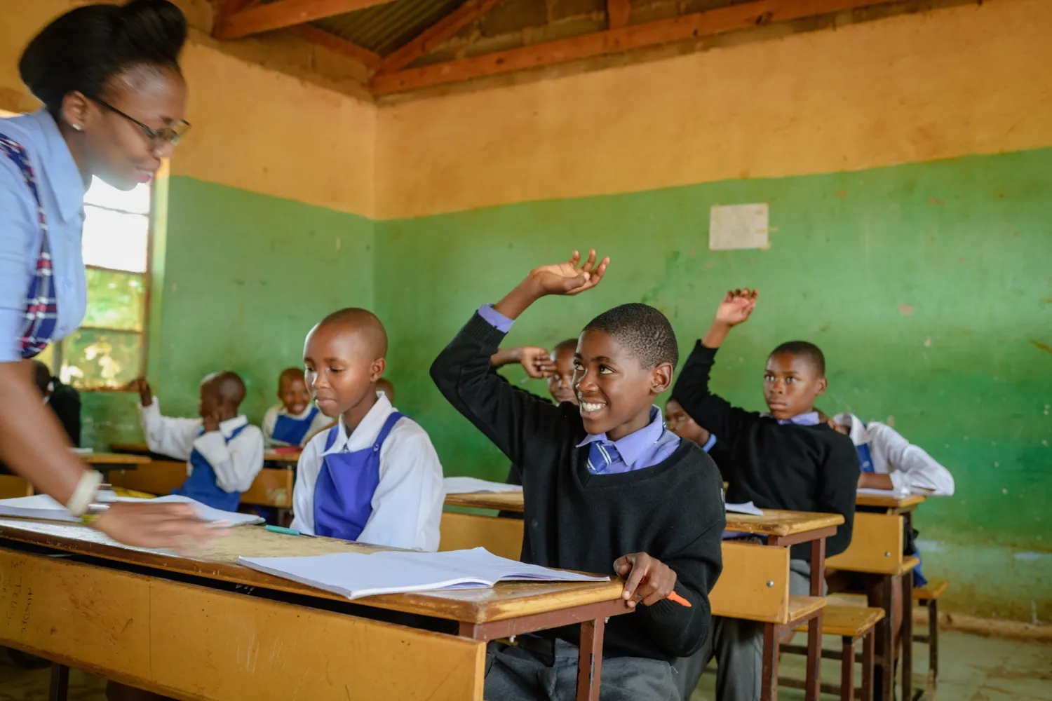 Female school teacher in classroom with smiling learner student hand raised