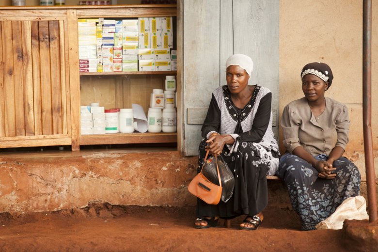 Two women in Uganda sitting by a small pharmacy