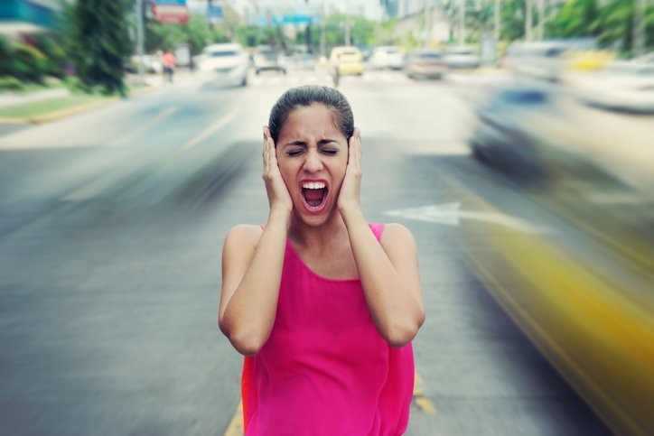 Woman standing on a street covering her ears.