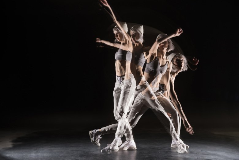 Woman in sports clothing dancing against black background