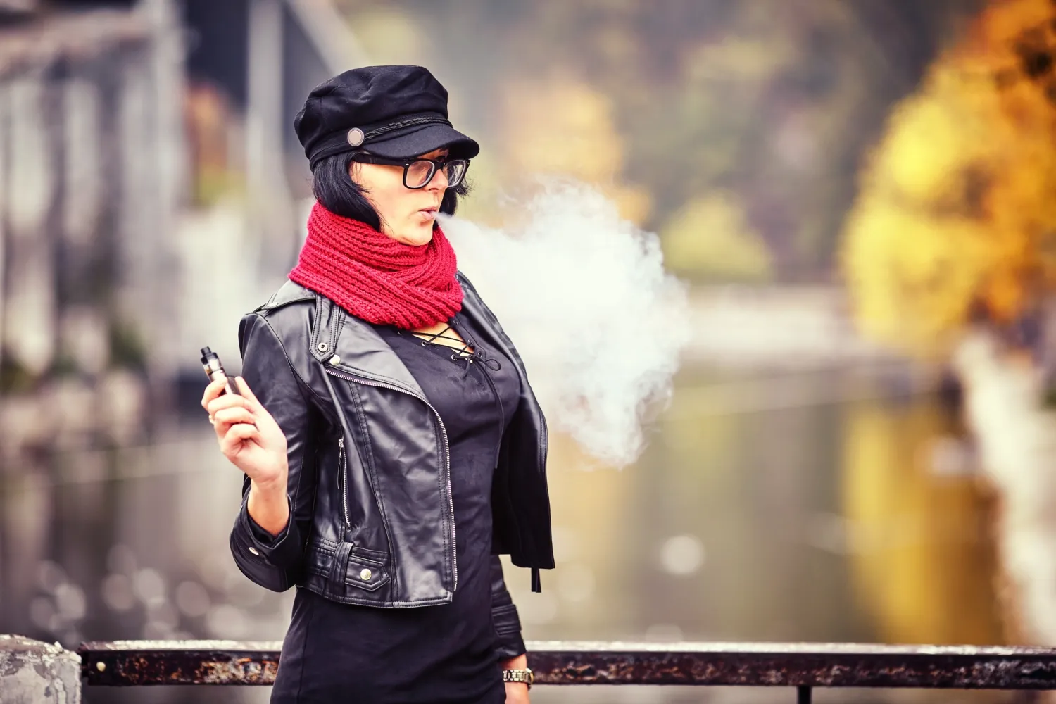 En ung kvinna i svart jacka och med solglasögon röker en e-cigarett.