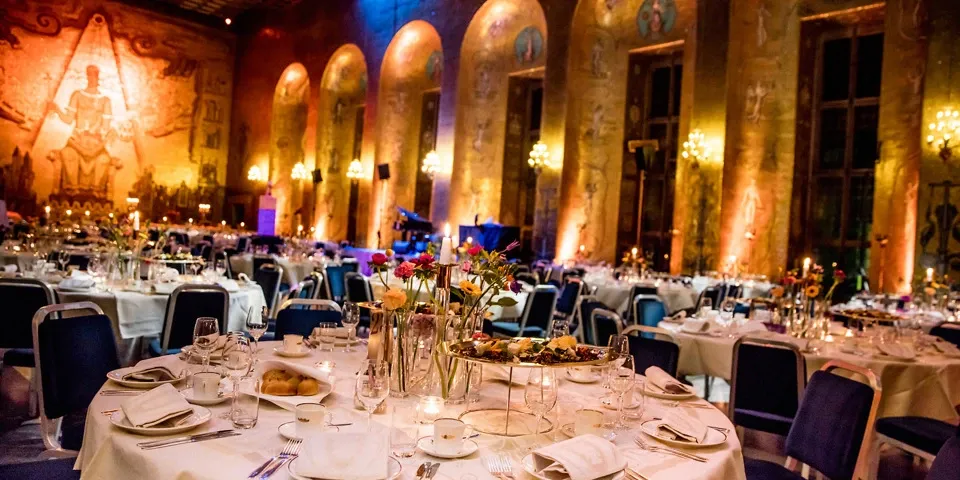 Picture of round tables set with white tablecloths in the Golden Hall in Stockholm City Hall.