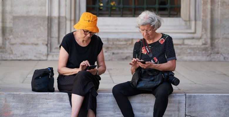 Two old women using their smart phones in  a vacation setting.