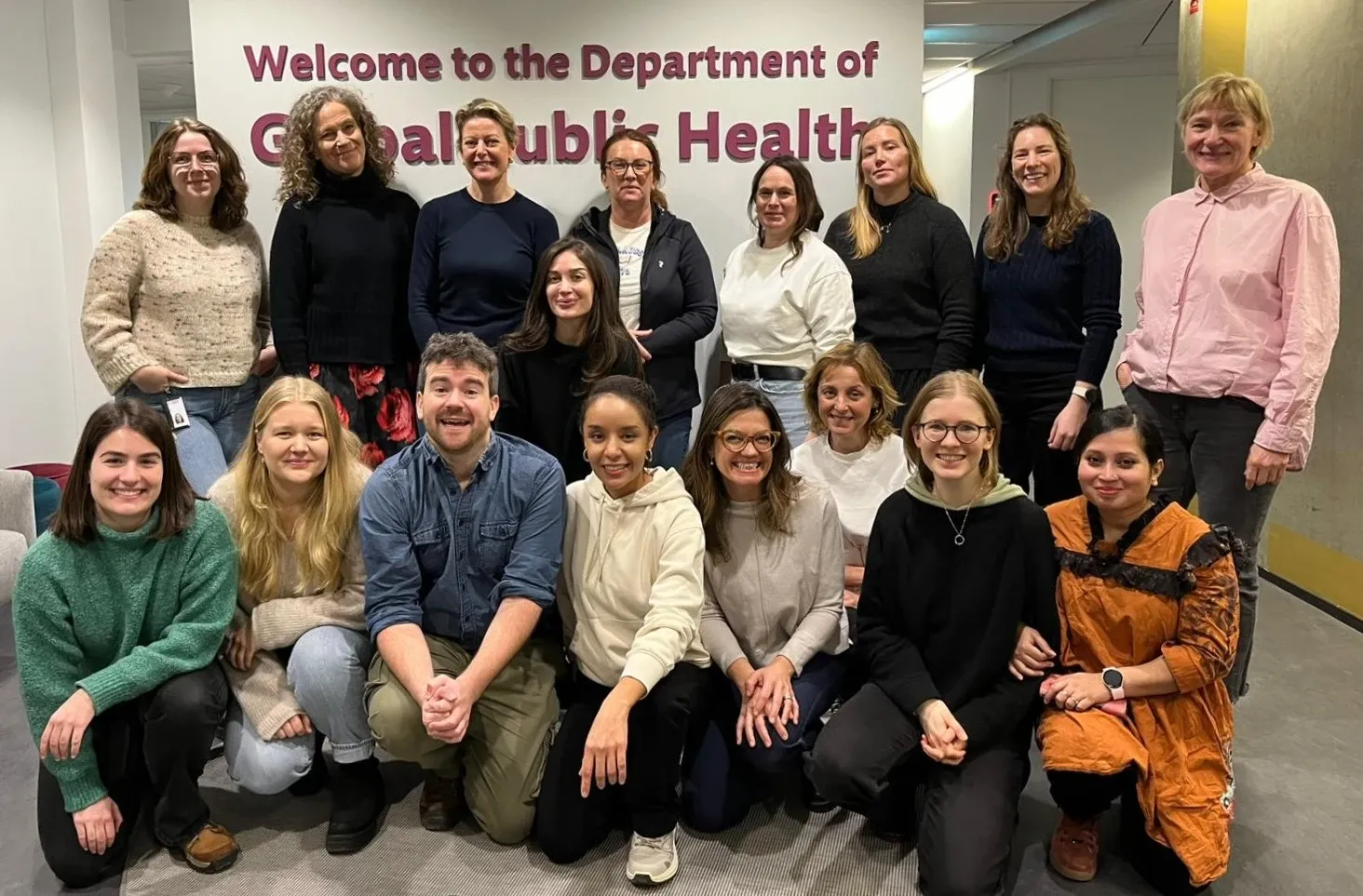 A group of people standing in front of a wall with a sign that says Department of Global Public Health