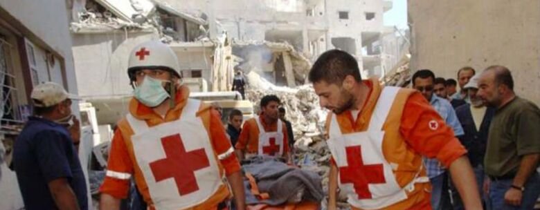 Two men in white vests with red crosses on carry a stretcher
