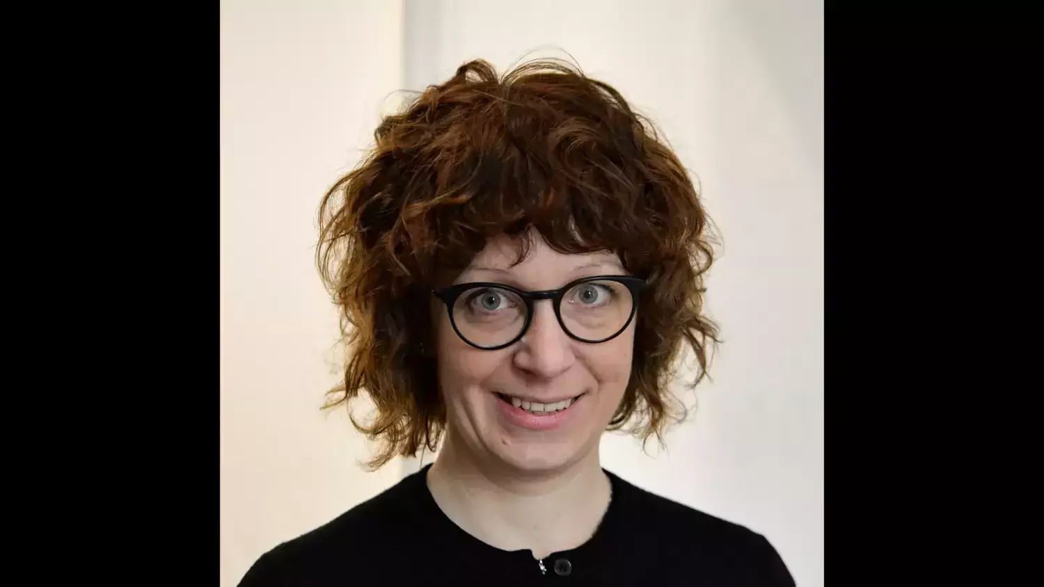 Profilfoto på Hedvig Glans. En kvinna med rött lockigt hår och svart tröja