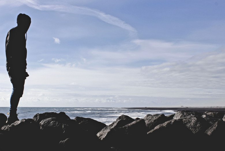 A person is standing by the shore looking at the sea