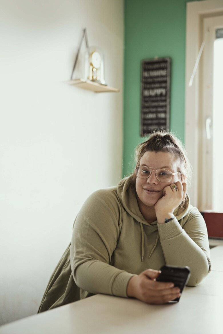 En kvinna som bär glasögon och sitter med telefonen.