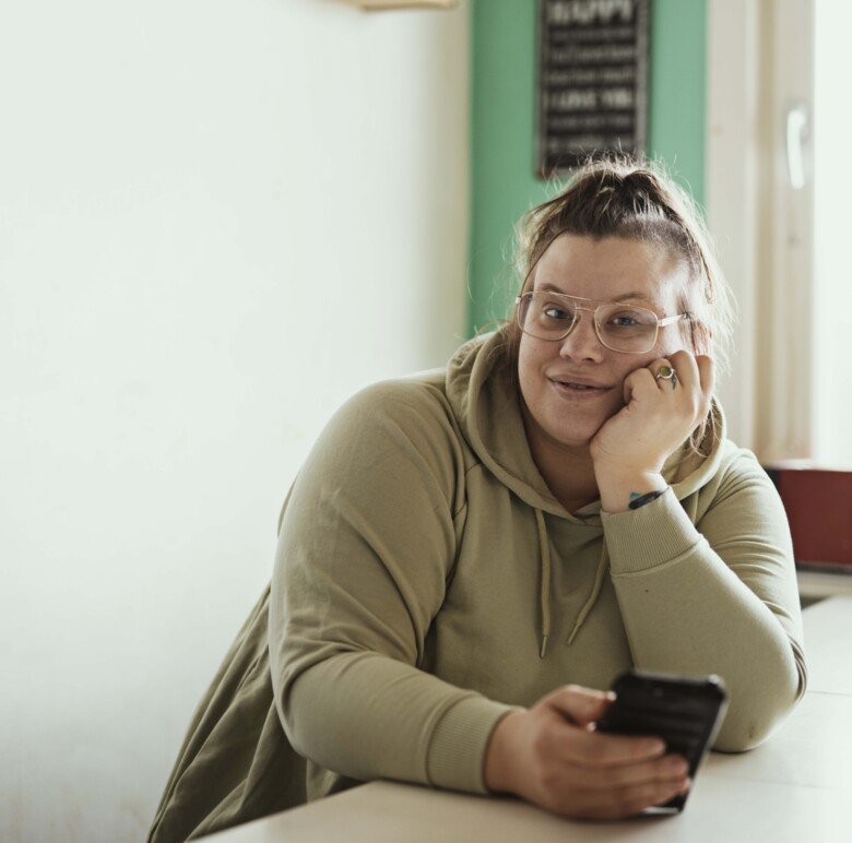 En kvinna som bär glasögon och sitter med telefonen.