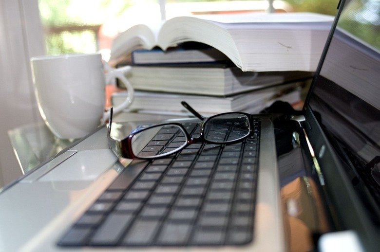 Skrivbort med ett tangentbord, böcker och ett par glasögon