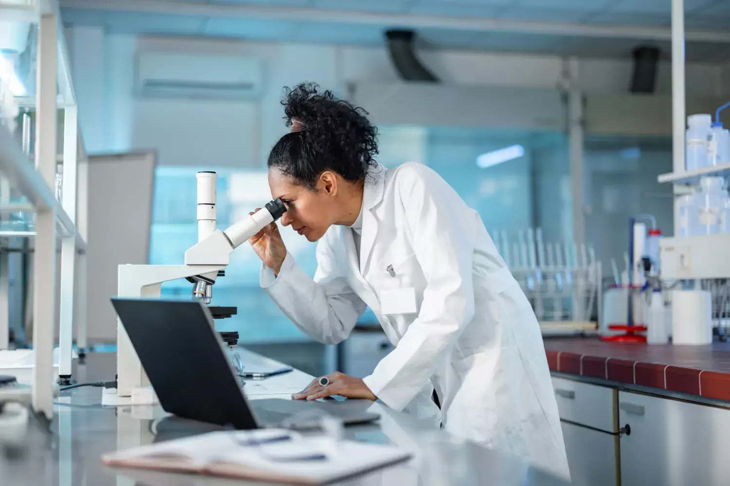 Woman in a lab looks in to a microscope.