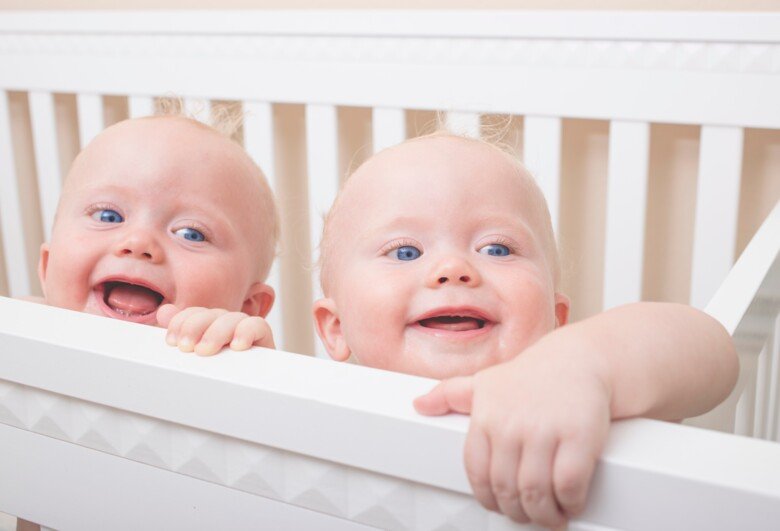 Två 9-månaders identiska tvillingpojkar som står upp i sin säng och skrattar