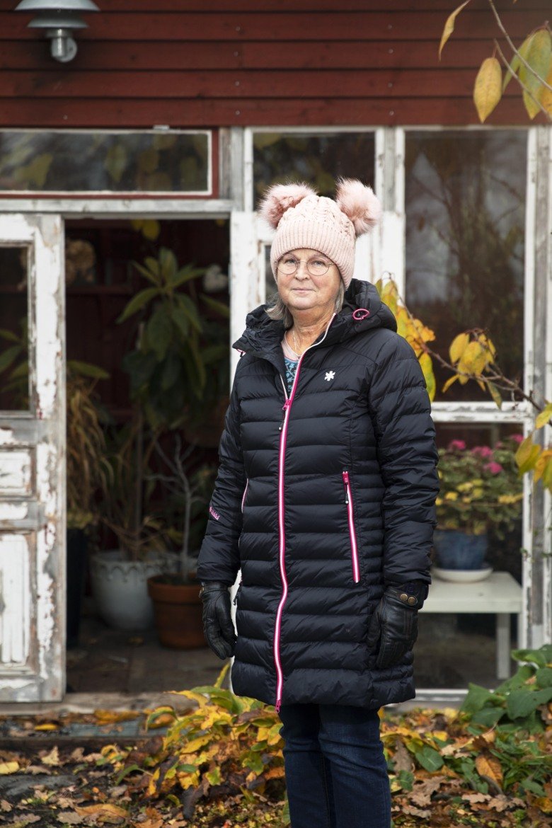 Monica Holmner som står utomhus framför sitt hus, det finns löv på marken.