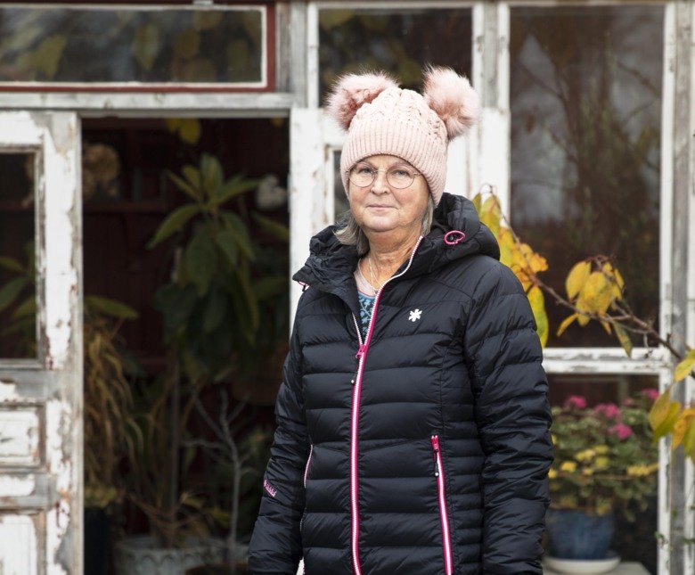 Monica Holmner som står utomhus framför sitt hus, det finns löv på marken.