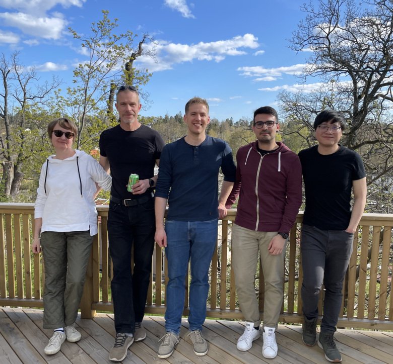 Five people standing next to each other smiling infront of the camera for a group photo.