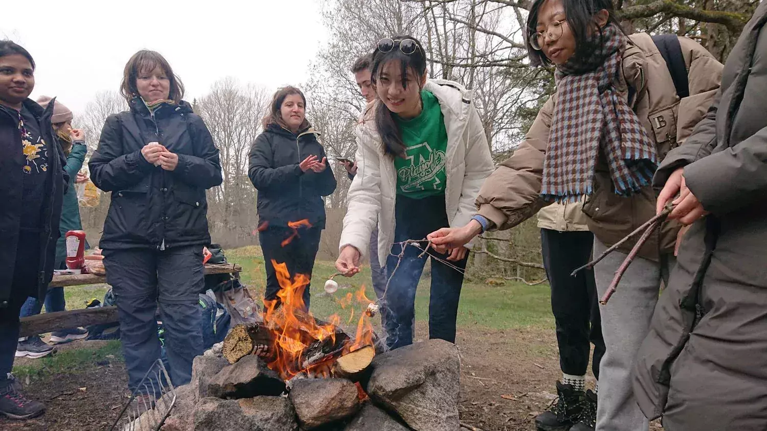 People barbecuing sausages over open fire outdoors.