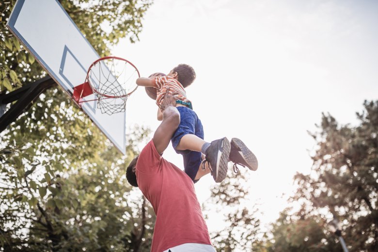A dad lifting his son on a basketball court