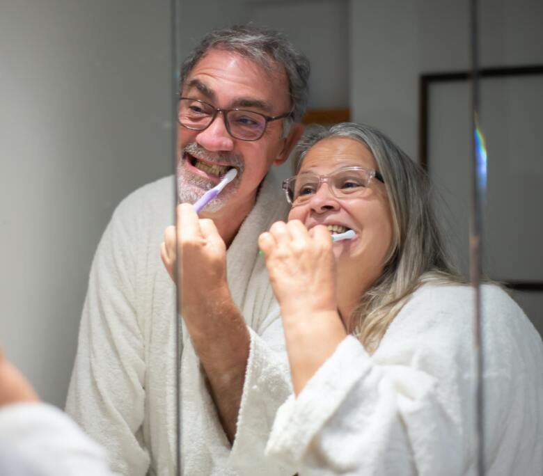 Ett äldre par står i badrummet framför spegeln och borstar tänderna tillsammans