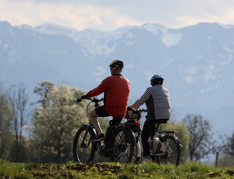 Two elderly people cycling in nature, they are both wearing helmets.