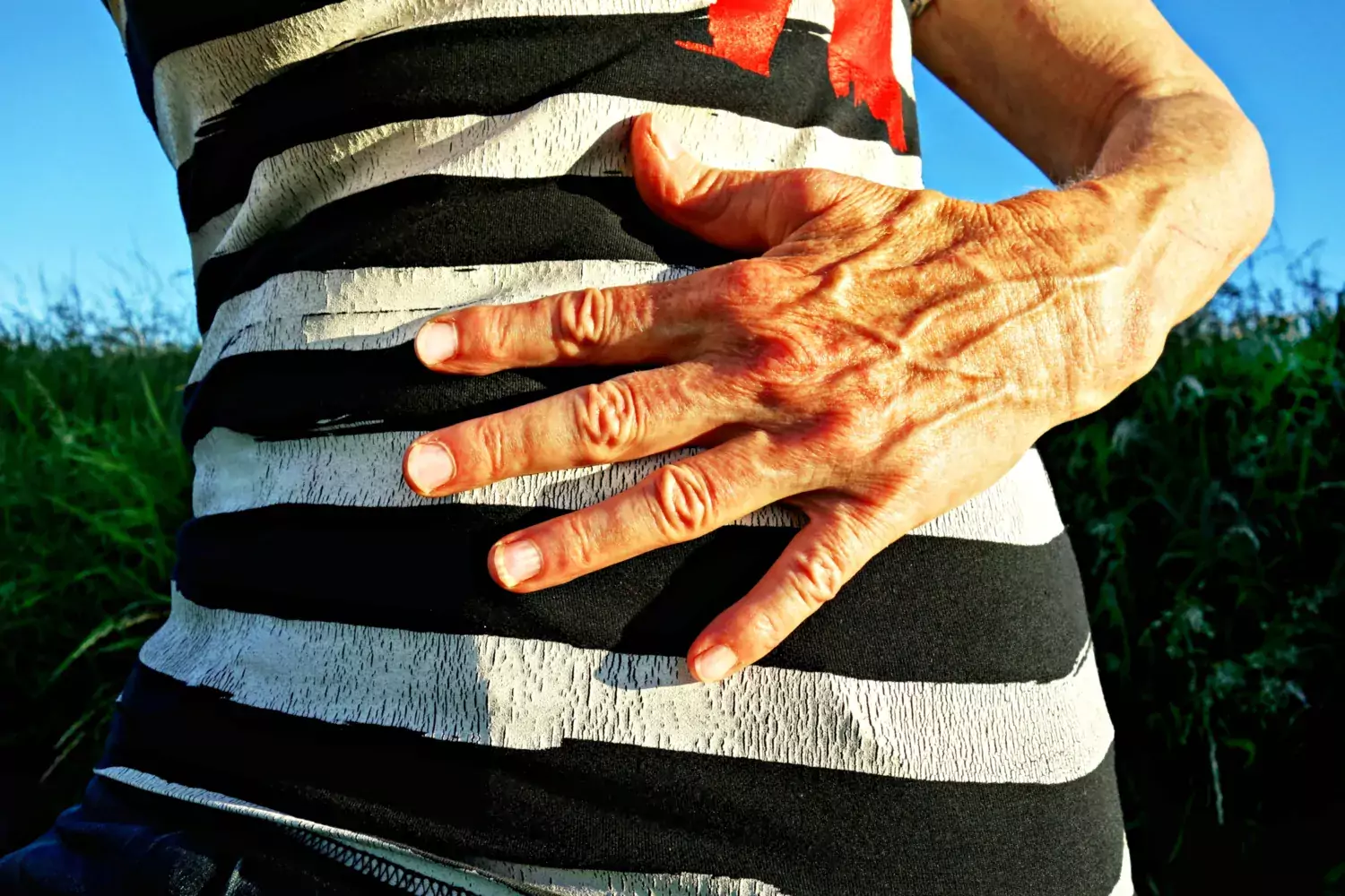 En äldre kvinna håller sin hand på maken. Hon är klädd i en randig tröja.