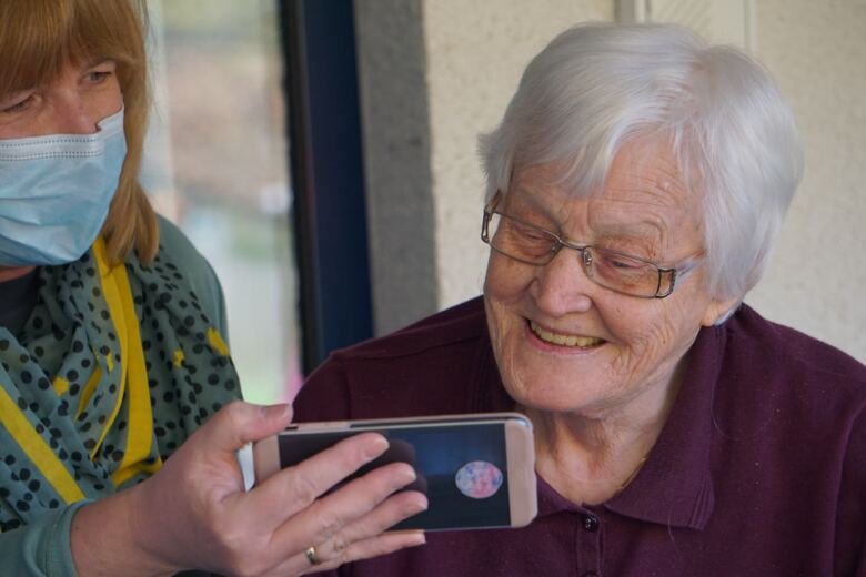 Kvinna visar äldre kvinna något på en mobiltelefon