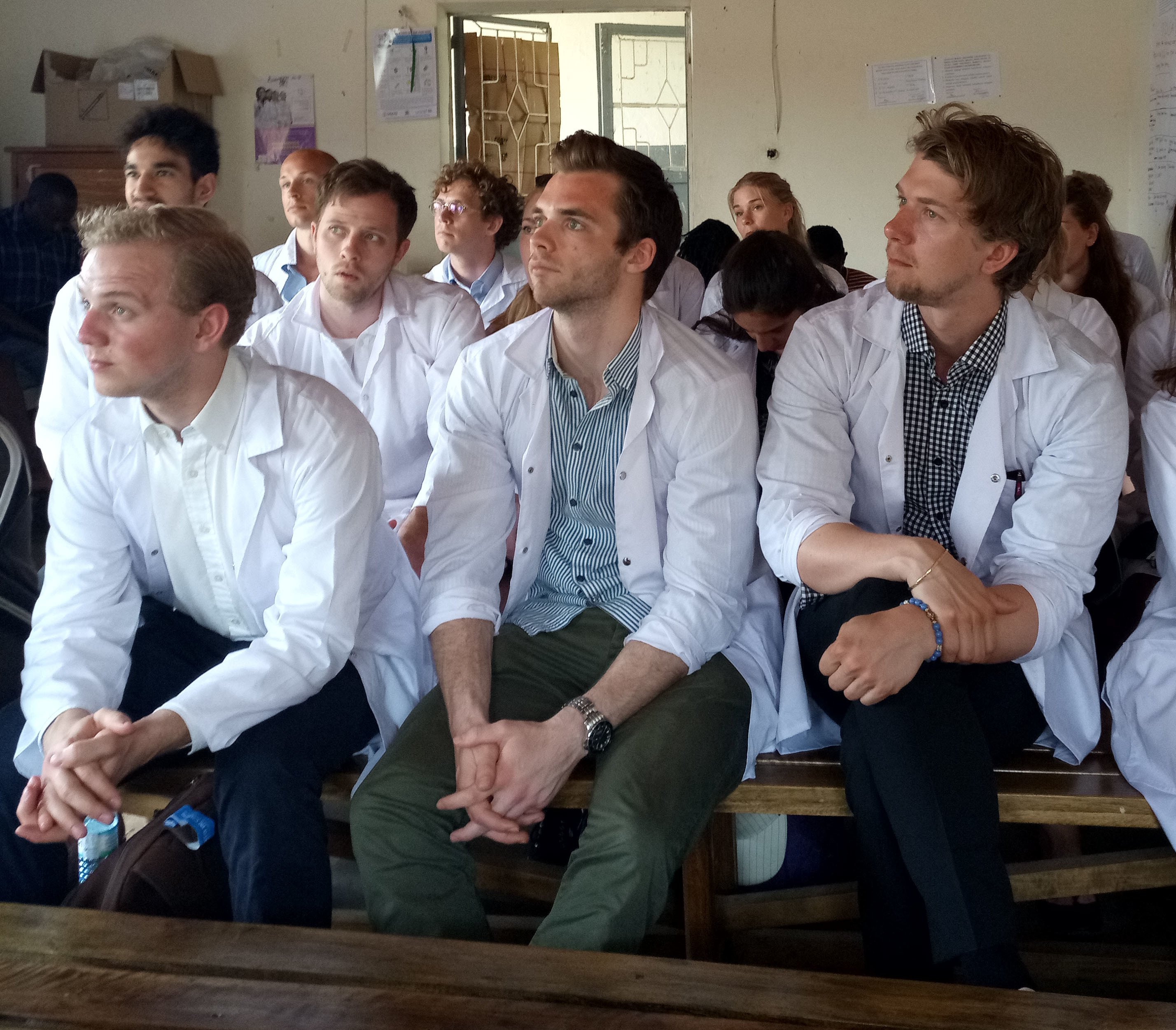 Students in white lab coats sitting on several rows listening attentively.