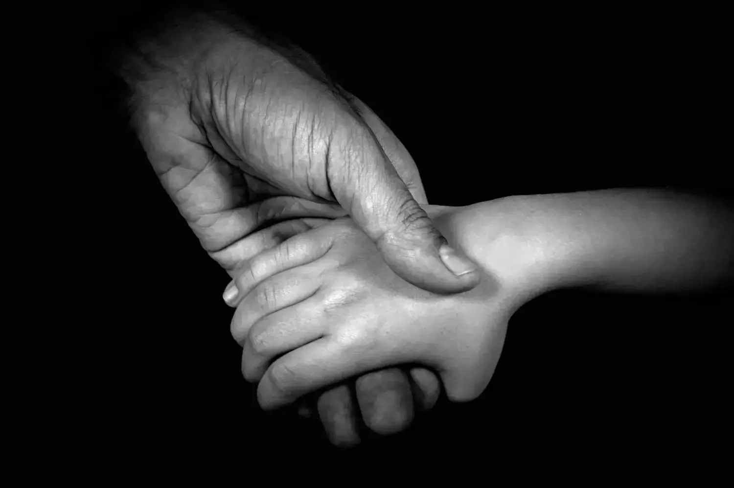 A hand of an adult person holding the hand of a child.